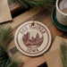 A decorative ornament featuring the skyline of Des Moines, Iowa, with a cup of coffee and pine branches in the background.