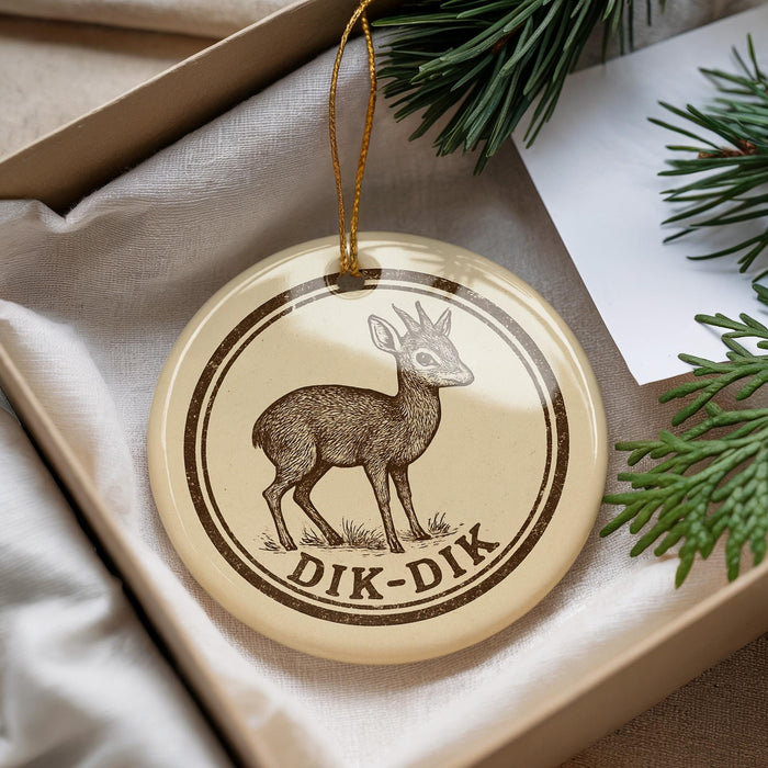 A round ornament with a deer image and the text "DIK-DIK" printed on it, placed in a box with pine branches.