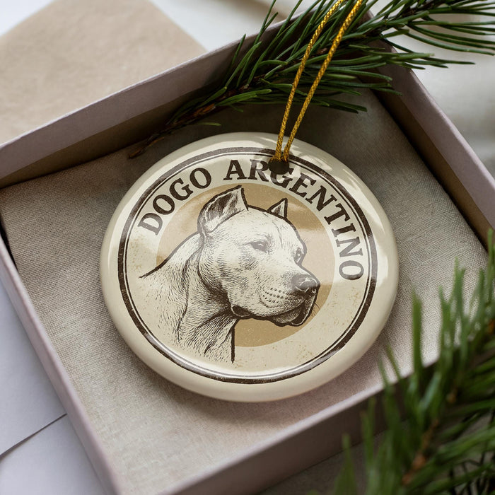 A circular ornament with a dog's head image and the text "DOGO ARGENTINO" printed on it, placed inside a box with pine branches.