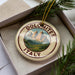 A decorative ornament with a mountain landscape and the text "DOLOMITES ITALY" on it, placed in a box with pine branches.
