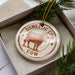 A decorative ornament in a box, featuring a cow illustration and the text "DOMESTIC COW" on a circular background.