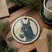 a ceramic ornament with a donkey's head design, placed on a wooden surface alongside a cup of coffee and some pine branches.