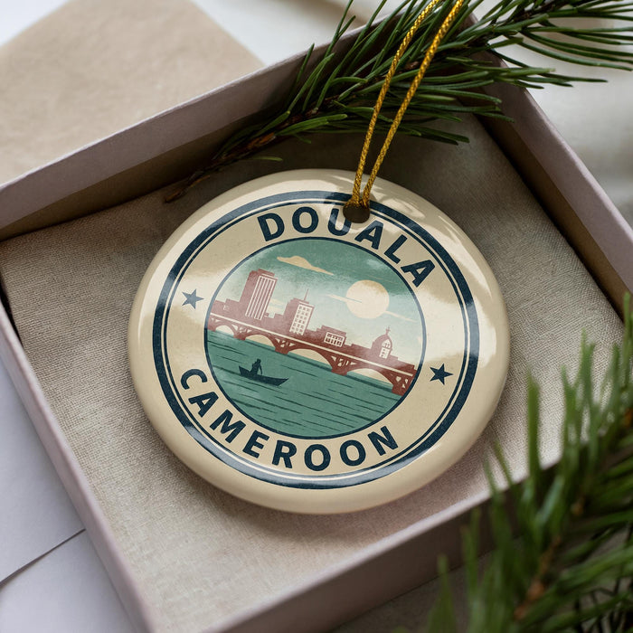 A circular ornament with the text "DOUALA CAMERON" and an illustration of a cityscape with a bridge, hanging from a string.