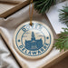 A decorative ornament with the text "Dover Delaware" and an illustration of a building, placed on a surface with pine branches and a white paper.