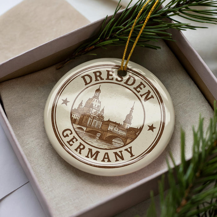 A circular ornament with the text "Dresden Germany" printed on it, surrounded by a decorative border and a pine branch.