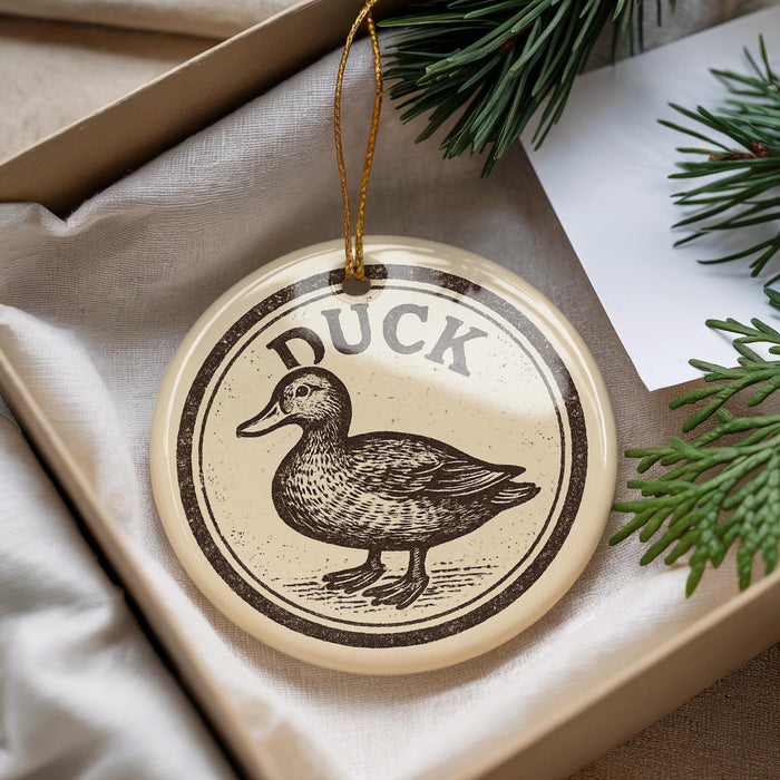 A decorative ornament featuring a duck is displayed in a box, surrounded by pine branches.