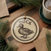 A ceramic ornament featuring a duck is displayed on a wooden surface, accompanied by a cup of coffee and pine branches.