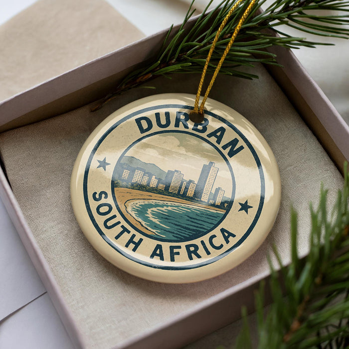 A decorative ornament with the text "DURBAN SOUTH AFRICA" and a cityscape image, placed in a box with pine branches.
