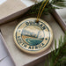 A decorative ornament with the text "DURBAN SOUTH AFRICA" and a cityscape image, placed in a box with pine branches.