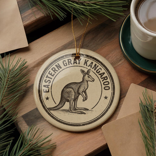 A circular ornament featuring a kangaroo, with the text "EASTERN GRAY KANGAROO" around the edge, is displayed on a wooden surface alongside a cup of coffee and some pine branches.
