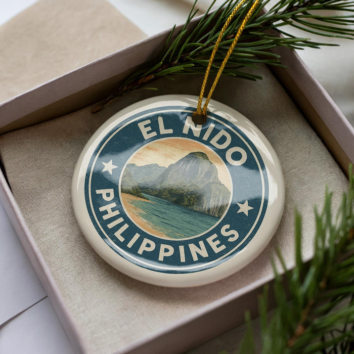A round ornament with the text "EL NIDO PHILIPPINES" and a mountain landscape design, placed in a box with pine branches.