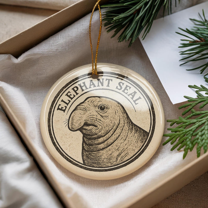 A circular ornament featuring an elephant seal, with the text "Elephant Seal" printed on it, is displayed in a box with pine branches.
