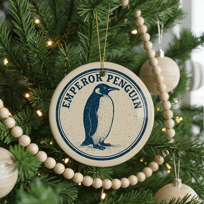A round ornament on a Christmas tree featuring a penguin design, with the text "EMPOROR PENGUIN" printed on it.