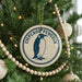 A round ornament on a Christmas tree featuring a penguin design, with the text "EMPOROR PENGUIN" printed on it.