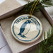 A round ornament with a penguin image and the word "EMPOROR PENGUIN" printed on it, hanging from a string.