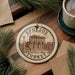 A circular ornament with the text "EPHESUS TURKEY" and an illustration of the ancient city of Ephesus, Turkey, is displayed on a wooden surface.