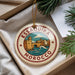 A decorative ornament with the text "ESSAOURA MAROCCO" and an illustration of a cityscape, placed in a box with pine branches.