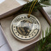 A ceramic ornament in a box, featuring a dog's face surrounded by stars and the text "ESTRELLA MOUNTAIN DOG".