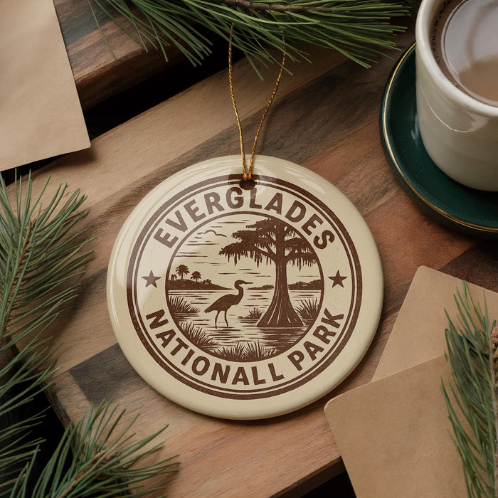 A circular ornament with the text "EVERGLADES NATIONAL PARK" printed on it, surrounded by pine branches and a cup of coffee on a wooden surface.