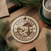 A circular ornament with the text "EVERGLADES NATIONAL PARK" printed on it, surrounded by pine branches and a cup of coffee on a wooden surface.