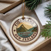 A decorative ornament with the text "FIORLAND NATIONAL PARK" and a mountain landscape design, placed in a box with pine branches.