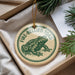 A round ornament with a green frog image and the text "FIRE-BELLIED TOAD" printed on it, hanging from a string.