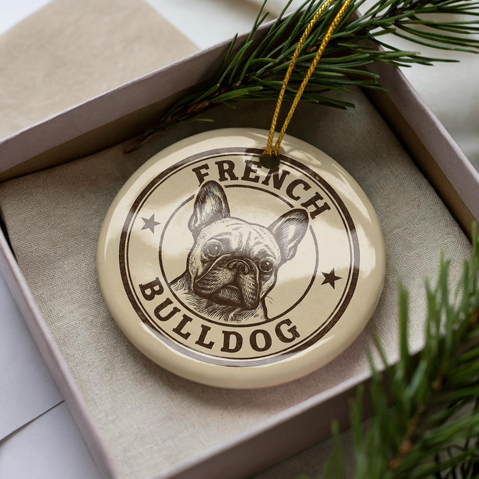 A circular ornament featuring a bulldog's face, with the text "FRENCH BULLDOG" printed on it, is displayed in a box surrounded by pine branches.