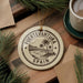 a circular ornament with the text "FUERTEVENTURA SPAIN" on it, surrounded by pine branches and a cup of coffee.