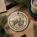 A circular ornament with the text "GABORONE BOTSWANA" printed on it, surrounded by pine branches and a cup of coffee on a wooden surface.