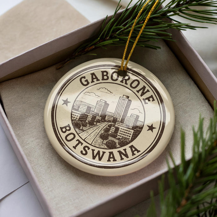 A circular ornament with the text "GABORONE BOTSWANA" printed on it, surrounded by a decorative border and a pine branch.