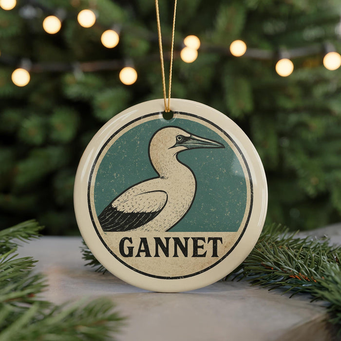 A circular ornament with a bird image and the word "GANNET" written on it, hanging in front of a Christmas tree with twinkling lights.