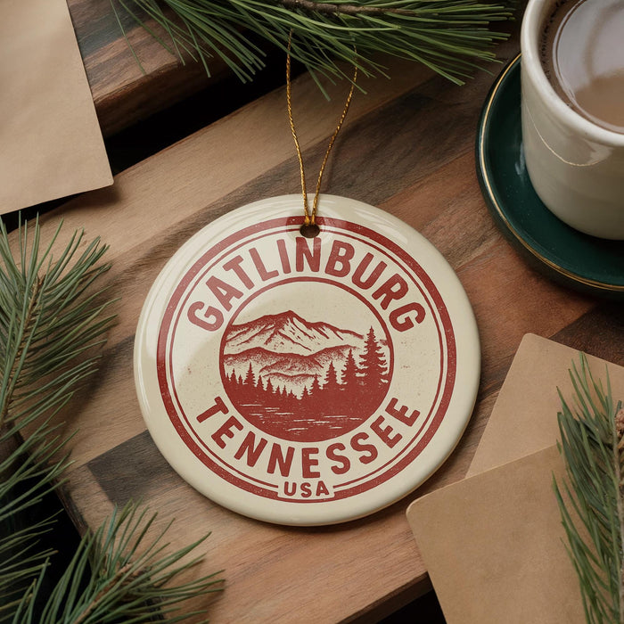 A circular ornament with the text "GATLINBURG TENNESSEE USA" printed on it, surrounded by pine branches and a cup of coffee on a wooden surface.