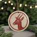 A round ornament featuring a red and white deer head design is displayed in front of a blurred Christmas tree with twinkling lights.