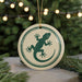 A round ornament with a green lizard design is displayed against a blurred background of a Christmas tree with lights.