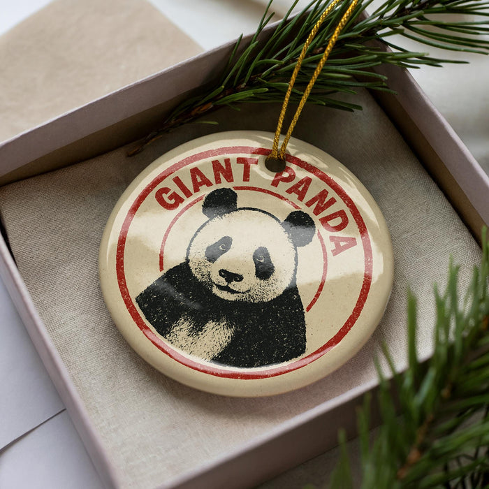 A circular ornament with a panda bear image and the text "GIANT PANDA" printed on it, placed inside a box with pine branches.