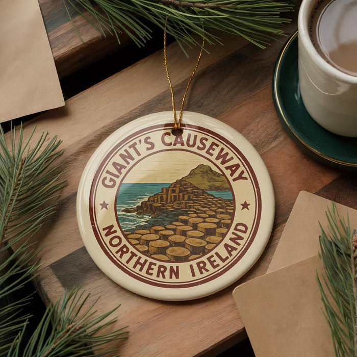 A circular ornament with the text "Giant's Causeway Northern Ireland" on it, surrounded by pine branches and a cup of coffee on a wooden surface.