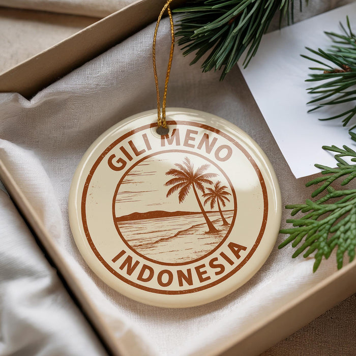 A round ornament with the text "GILI MENO INDONESIA" printed on it, surrounded by palm trees, is displayed in a box with pine branches.