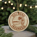 A circular ornament with the text "Gili Meno Indonesia" and a palm tree illustration, hanging from a string against a background of Christmas lights and greenery.