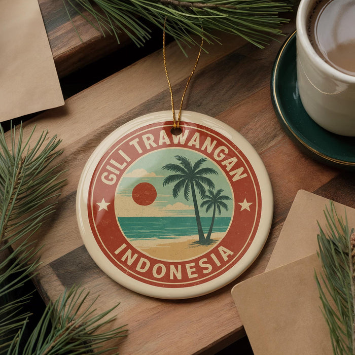 A circular ornament with a palm tree and beach scene, surrounded by pine branches, sits on a wooden surface.