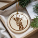 A decorative ornament featuring a giraffe's head is displayed in a box, surrounded by pine branches and greenery.