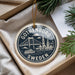 A decorative ornament with a circular design featuring a bridge and buildings, along with the text "GOThenburg, Sweden" printed on it. The ornament is hanging from a string and placed on a surface with some greenery visible in the background.