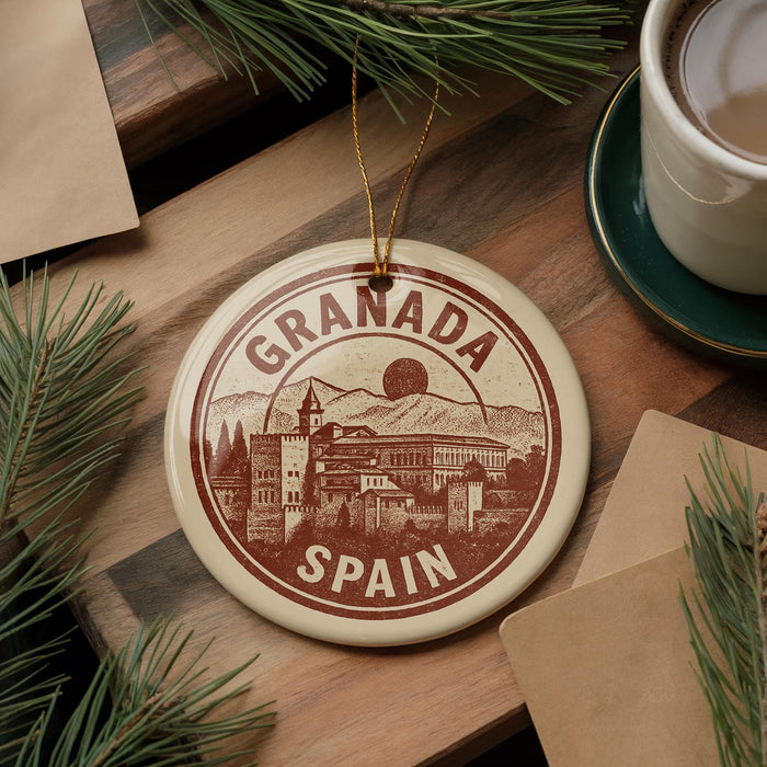 A circular ornament with the text "GRANADA SPAIN" is displayed on a wooden surface, surrounded by pine branches and a cup of coffee.