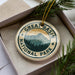 A circular ornament with the text "GREAT BASIN NATIONAL PARK" and a mountain landscape design, placed in a box with pine branches.