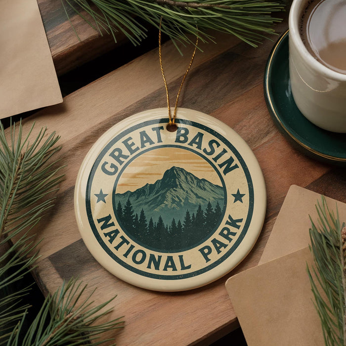 A circular ornament with the text "GREAT BASIN NATIONAL PARK" and a mountain landscape design, hanging on a wooden surface with pine branches and a cup of coffee nearby.