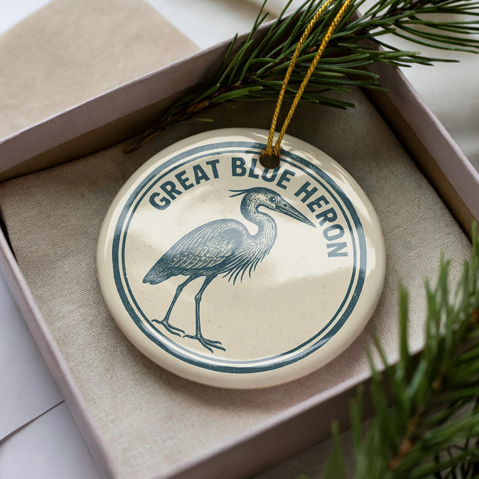 A circular ornament with a blue heron illustration and the text "GREAT BLUE HERON" on it, hanging from a string.