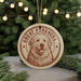 A circular ornament featuring a large brown dog with a smiling expression, surrounded by Christmas lights and greenery.