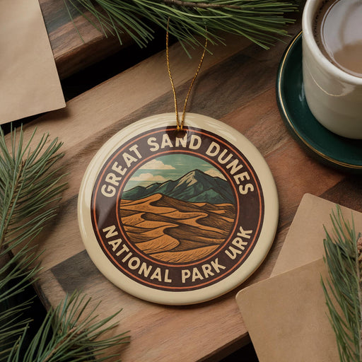 A circular ornament with the text "GREAT SAN DUNES NATIONAL PARK URK" is displayed on a wooden surface, surrounded by pine branches and a cup of coffee.