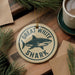 A circular ornament with the text "GREAT WHITE SHARK" and a graphic of a shark is displayed on a wooden surface, surrounded by pine branches and a cup of coffee.