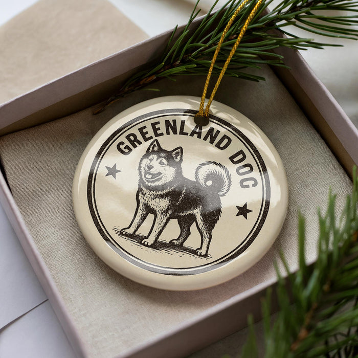 A circular ornament with a dog image and the text "GREENLAND DOG" on it, placed inside a box with pine branches.