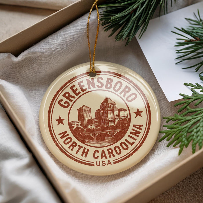 A circular ornament with the text "Greensboro North Carolina USA" printed on it, hanging from a string.
